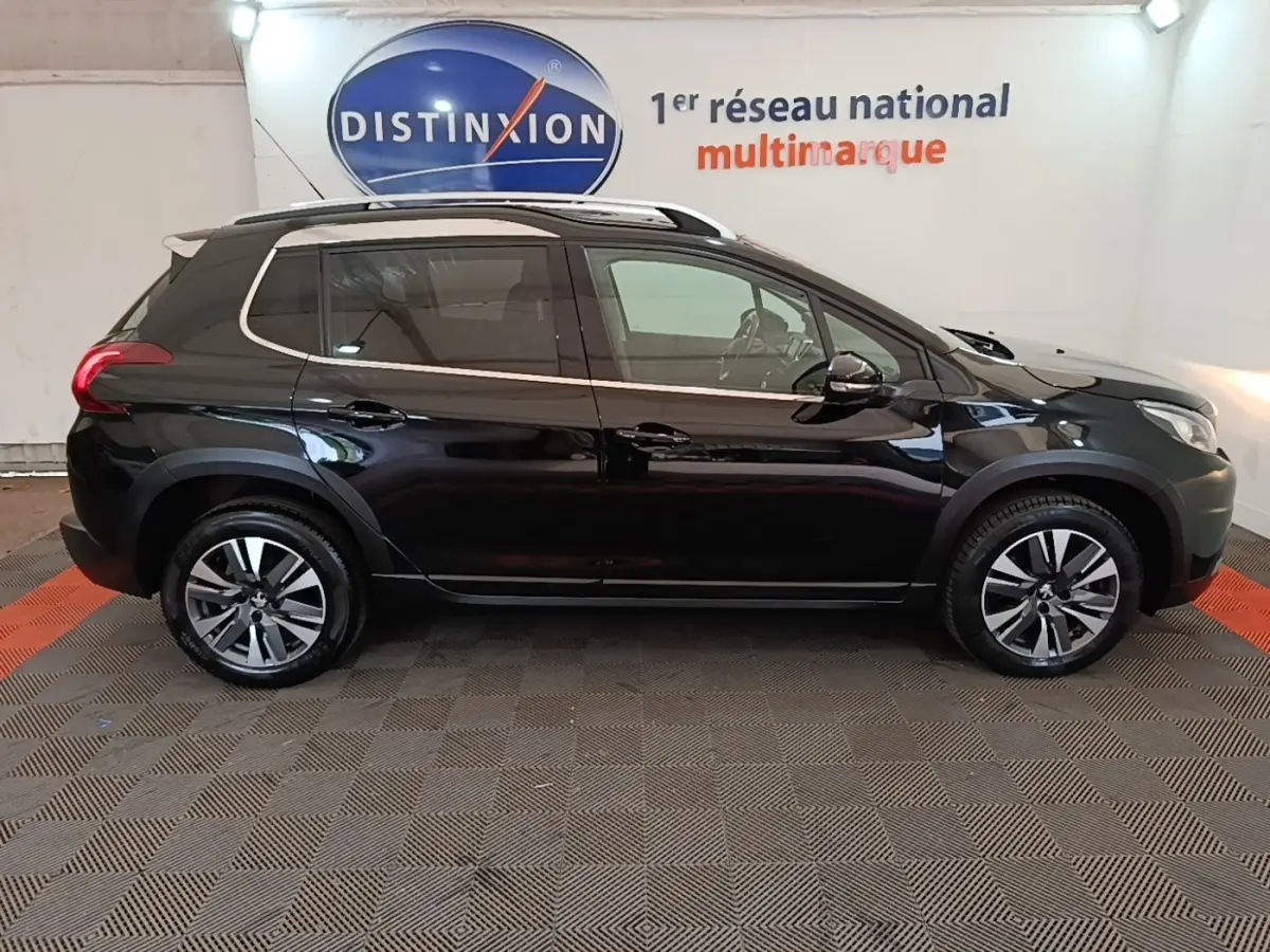 Profil droit d’un Peugeot 2008 noir 2019 avec jantes alliage et rails de toit chromés en intérieur showroom.