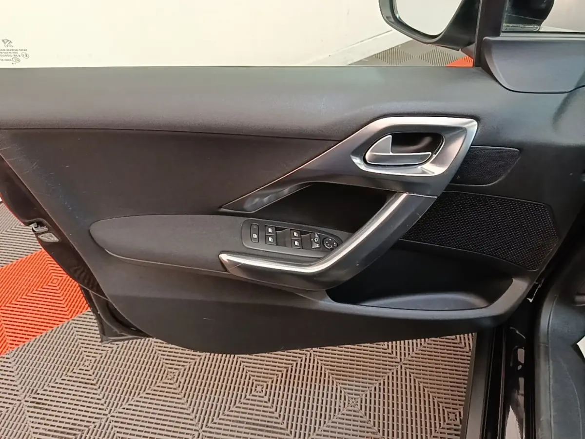 Vue côté intérieur de la porte avant gauche noire d'une Peugeot 2008 avec commandes des vitres et poignée argentée.