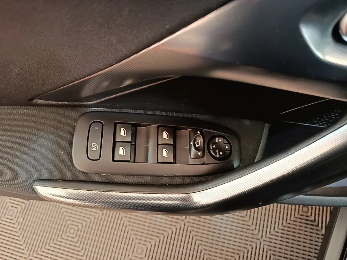 Gros plan sur les commandes des vitres et rétroviseurs côté gauche de la Peugeot 2008 noire, intérieur tissu.
