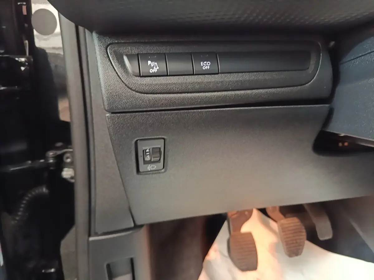 Vue intérieure côté gauche du tableau de bord noir du Peugeot 2008 avec commandes de phares et pédales visibles.
