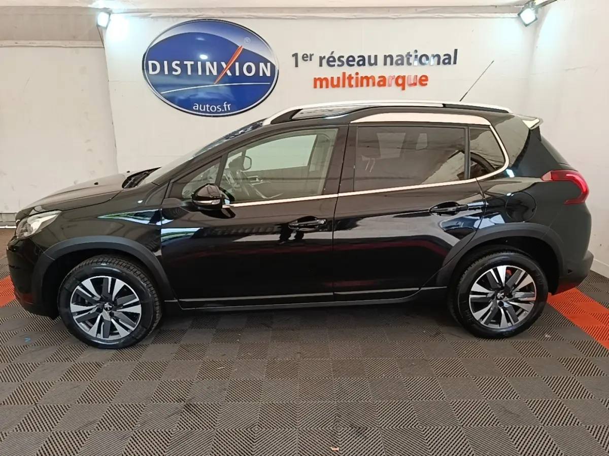 Profil côté gauche d'un Peugeot 2008 noir 2019 avec jantes alliage et barres de toit chromées en intérieur showroom.