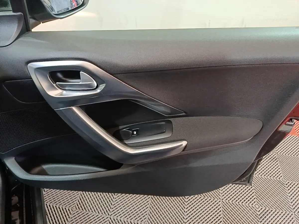 Intérieur de la porte côté conducteur d'une Peugeot 2008 noire, avec poignée argentée et commande de lève-vitre.