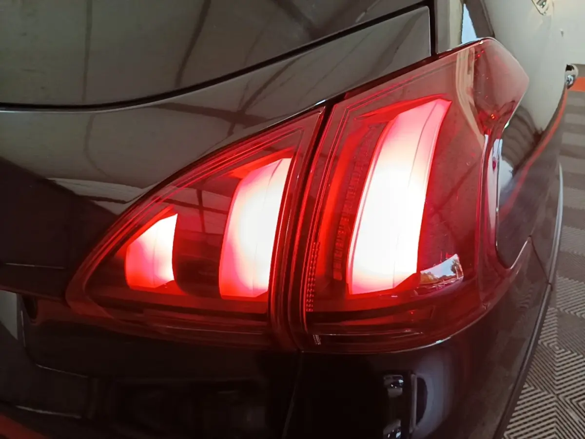Gros plan sur le feu arrière droit rouge d’une Peugeot 2008 noire, soulignant ses lignes modernes et brillantes.