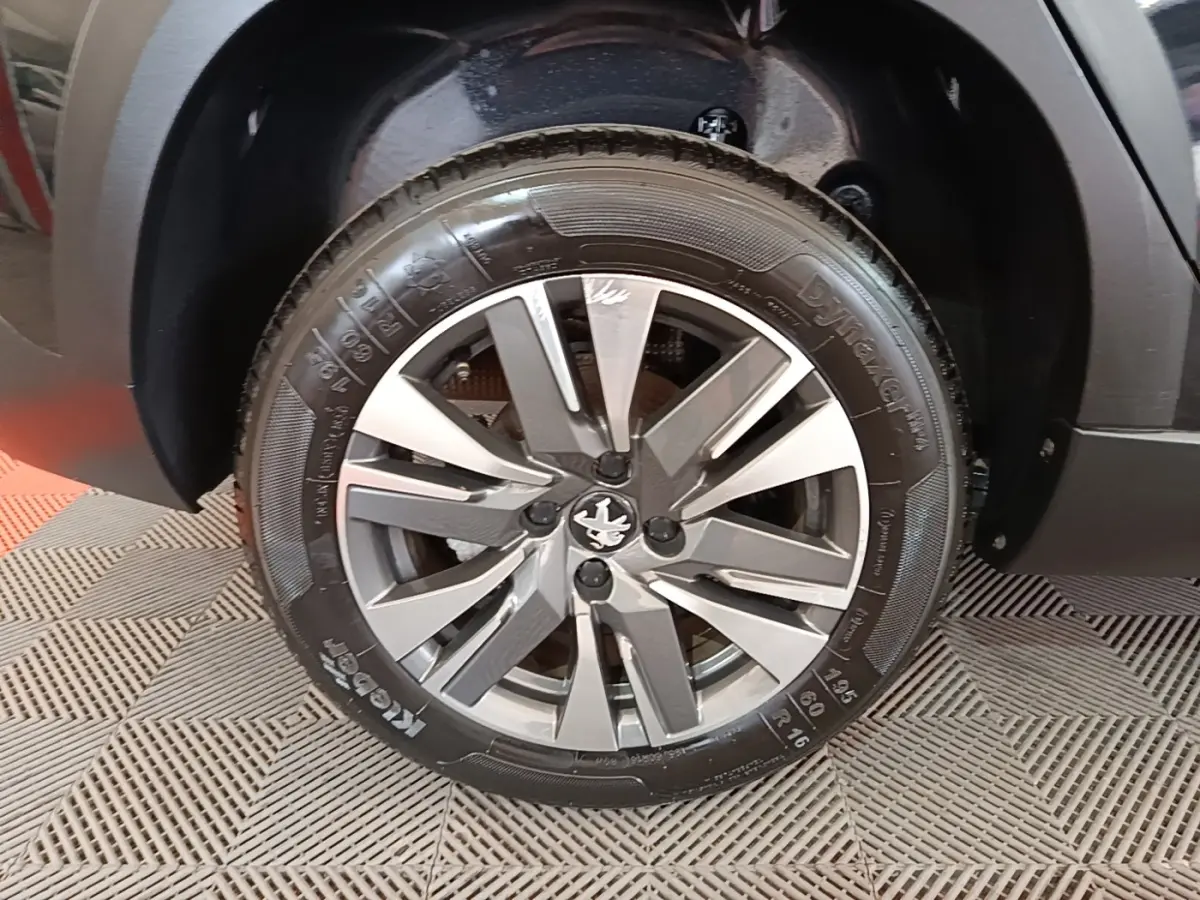 Gros plan sur la roue avant gauche noire d’un Peugeot 2008 avec jante alliage bicolore et logo lion central.
