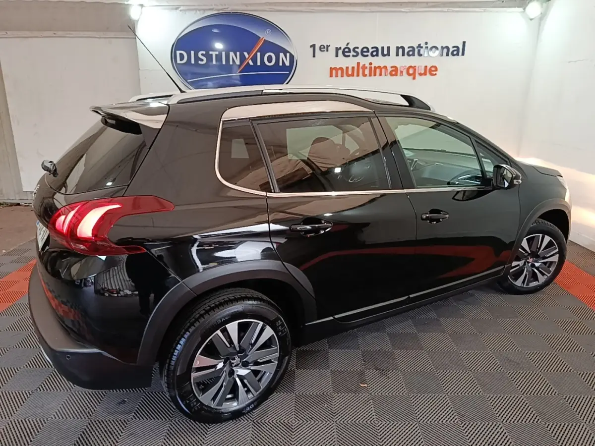 Vue 3/4 arrière droite d’un Peugeot 2008 noir brillant avec jantes alliage et rails de toit chromés en intérieur showroom.