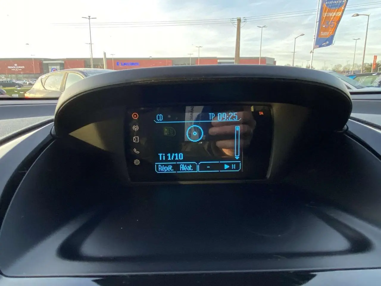 Écran central du tableau de bord de la Ford B-MAX blanc 2014 affichant les commandes audio avec vue extérieure floue.