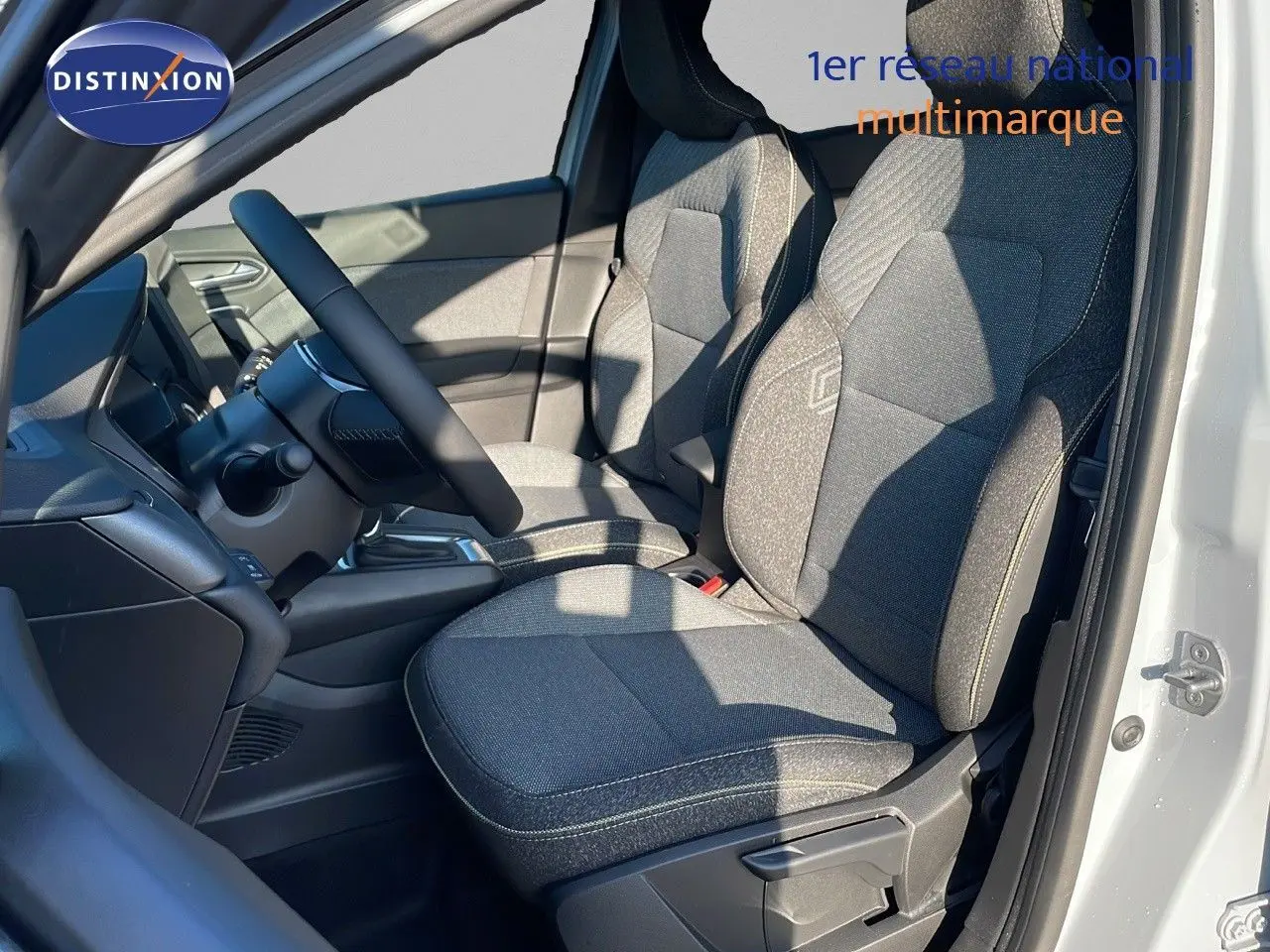 Intérieur avant droit du Renault Captur E-Tech hybride 2025 avec sièges gris et volant noir visible depuis la porte ouverte.