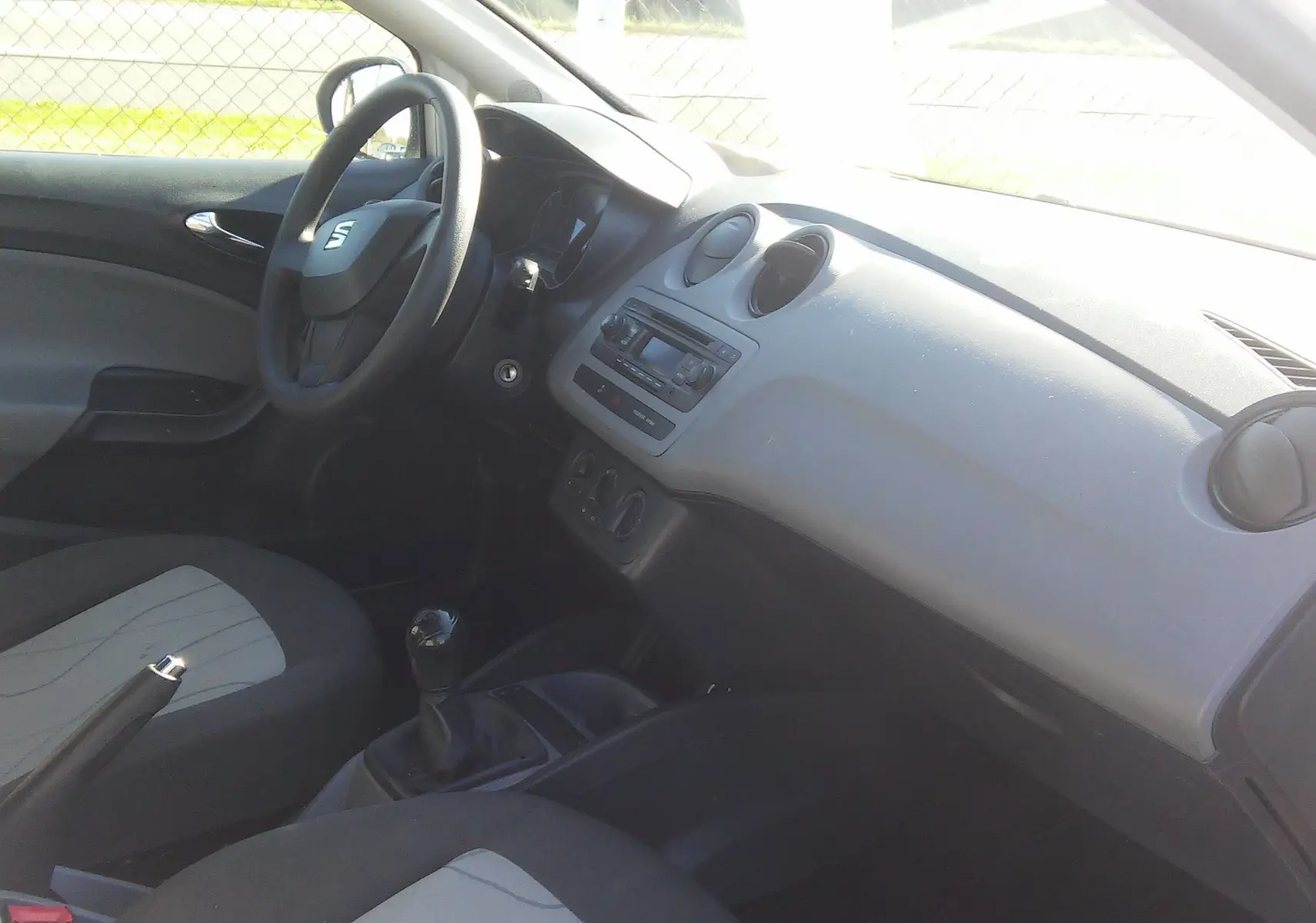 Intérieur de la SEAT Ibiza Business 2015 vu côté conducteur, tableau de bord gris et sièges noirs avec console manuelle.