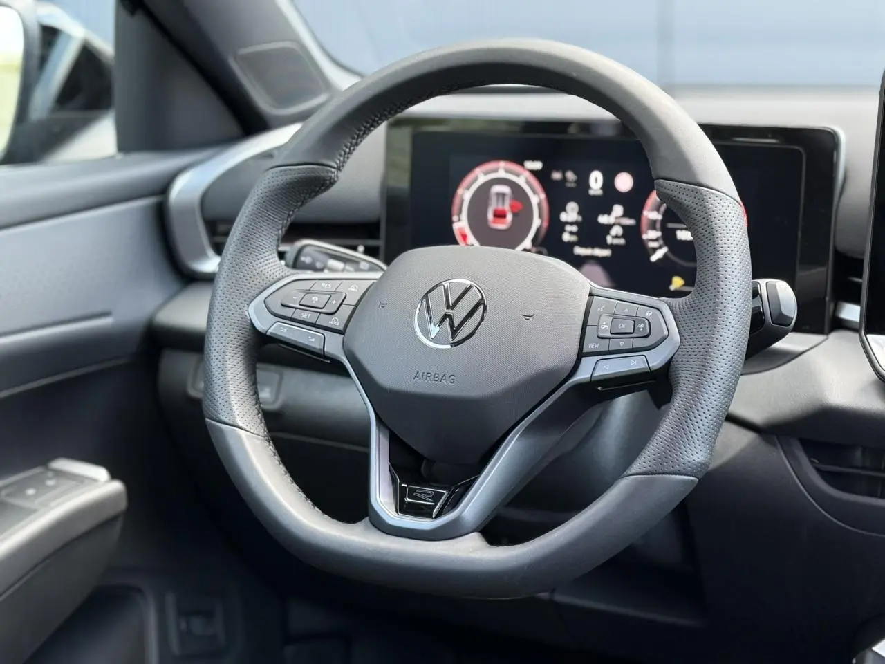 Volant sport multifonction en cuir noir avec logo Volkswagen, tableau de bord numérique en arrière-plan, intérieur T-Roc 2026.