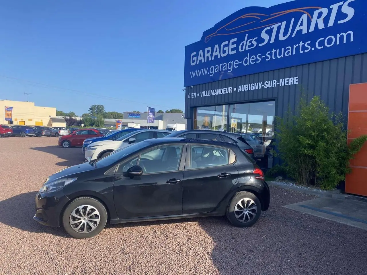 Peugeot 208 noire vue de profil côté gauche, garée devant un garage avec jantes acier 15 pouces et peinture métallisée.