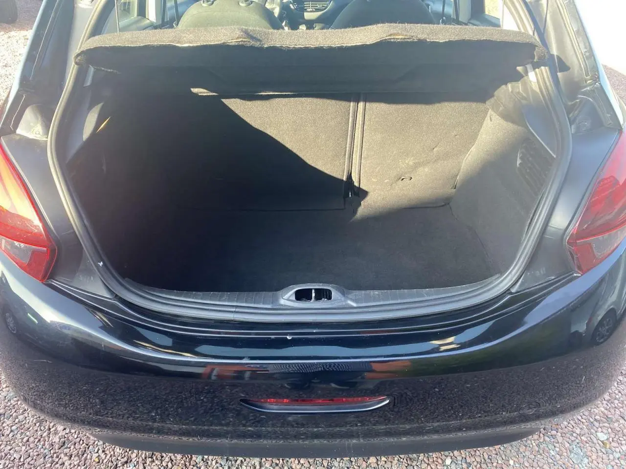 Coffre ouvert en vue arrière d'une Peugeot 208 noire de 2016, montrant l'espace de chargement vide.