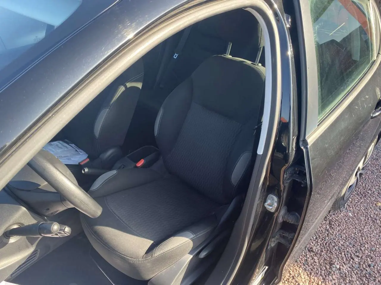 Vue intérieure côté conducteur de la Peugeot 208 noire de 2016, siège avant et volant multifonction visibles.