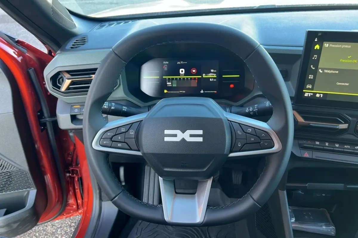 Vue intérieure centrée sur le volant du Dacia Duster 2024, avec tableau de bord numérique et écran tactile.