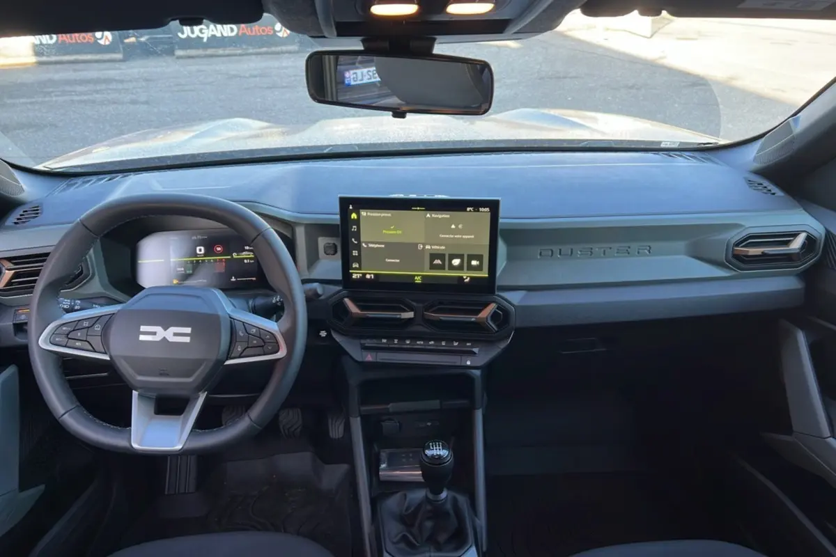 Vue intérieure du tableau de bord du Dacia Duster 2024 brun terracotta avec écran tactile et boîte manuelle visible.