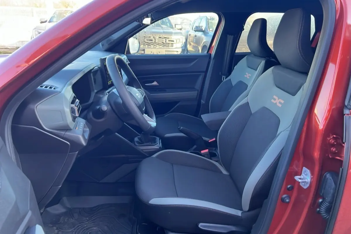 Vue intérieure côté conducteur du Dacia Duster 2024 brun terracotta, montrant les sièges sport et le tableau de bord moderne.