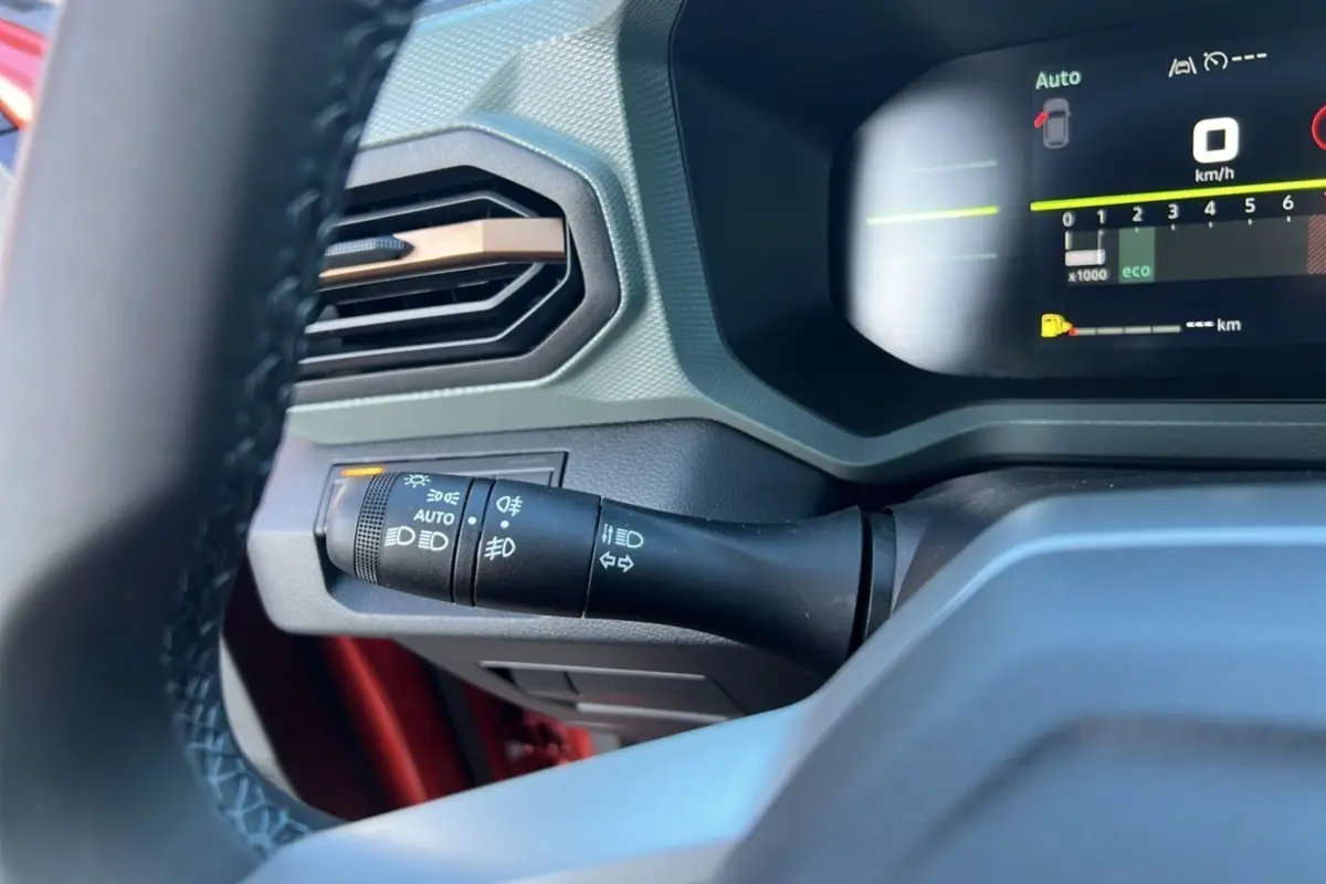 Détail du commodo d'éclairage et tableau de bord numérique du Dacia Duster 2024 brun terracotta, vue intérieure côté conducteur.