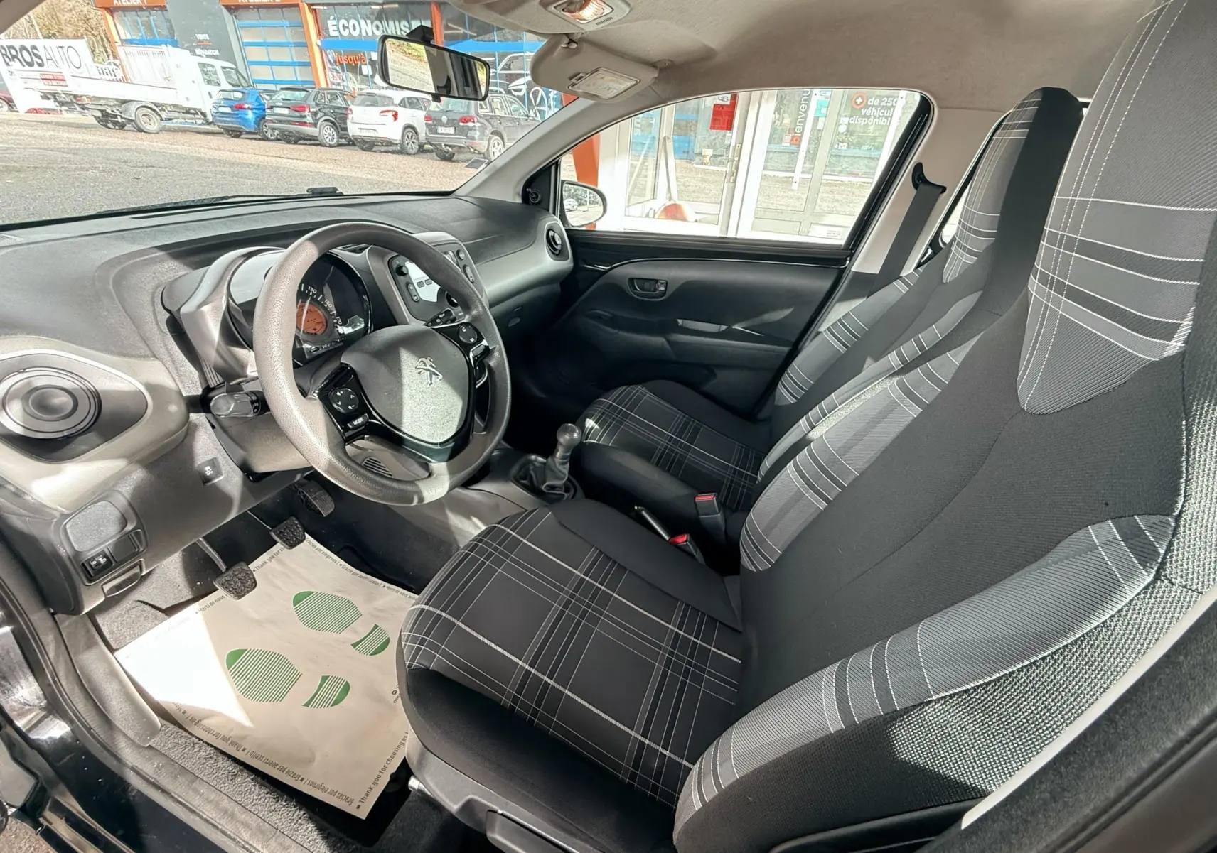 Intérieur avant droit de Peugeot 108 noir 2018, sièges tissu gris à motifs carreaux et volant multifonction.