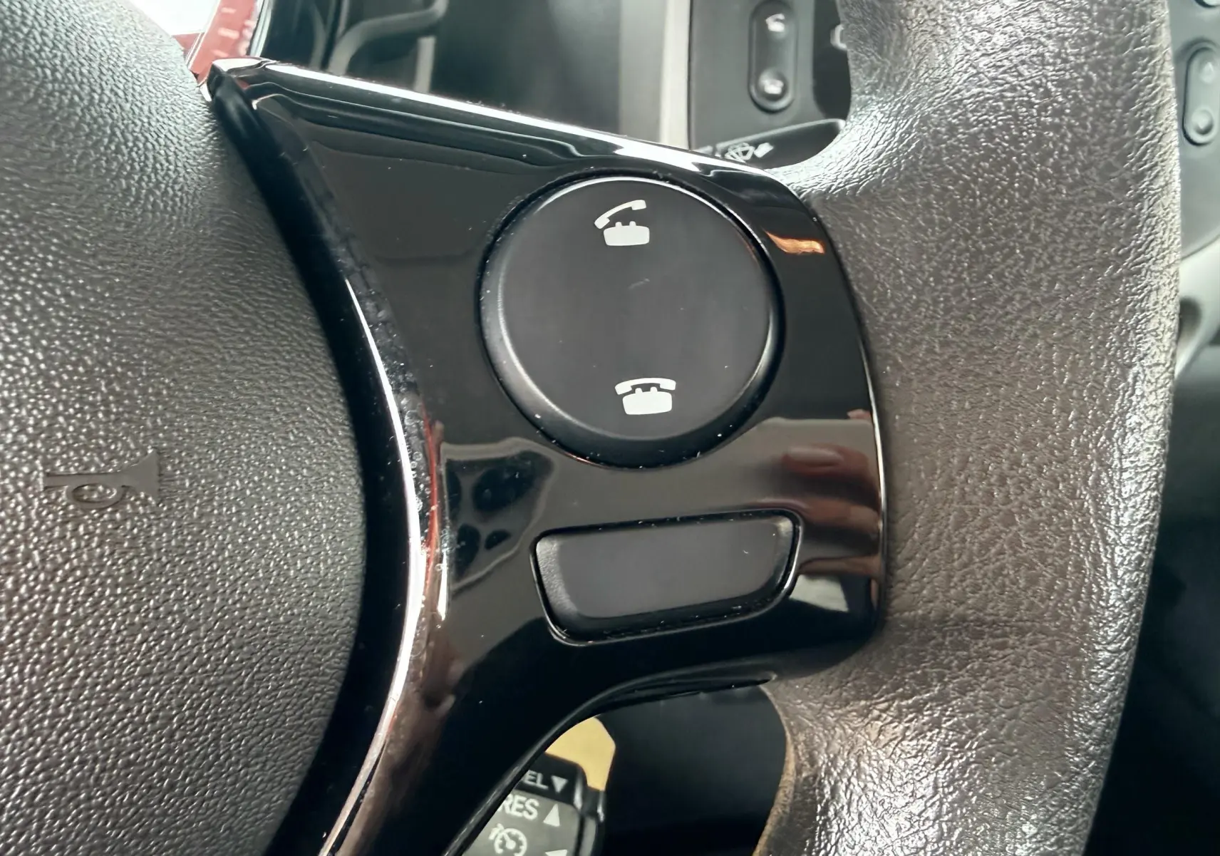 Gros plan sur les commandes téléphoniques noires intégrées au volant en cuir d'une Peugeot 108 noire de 2018.