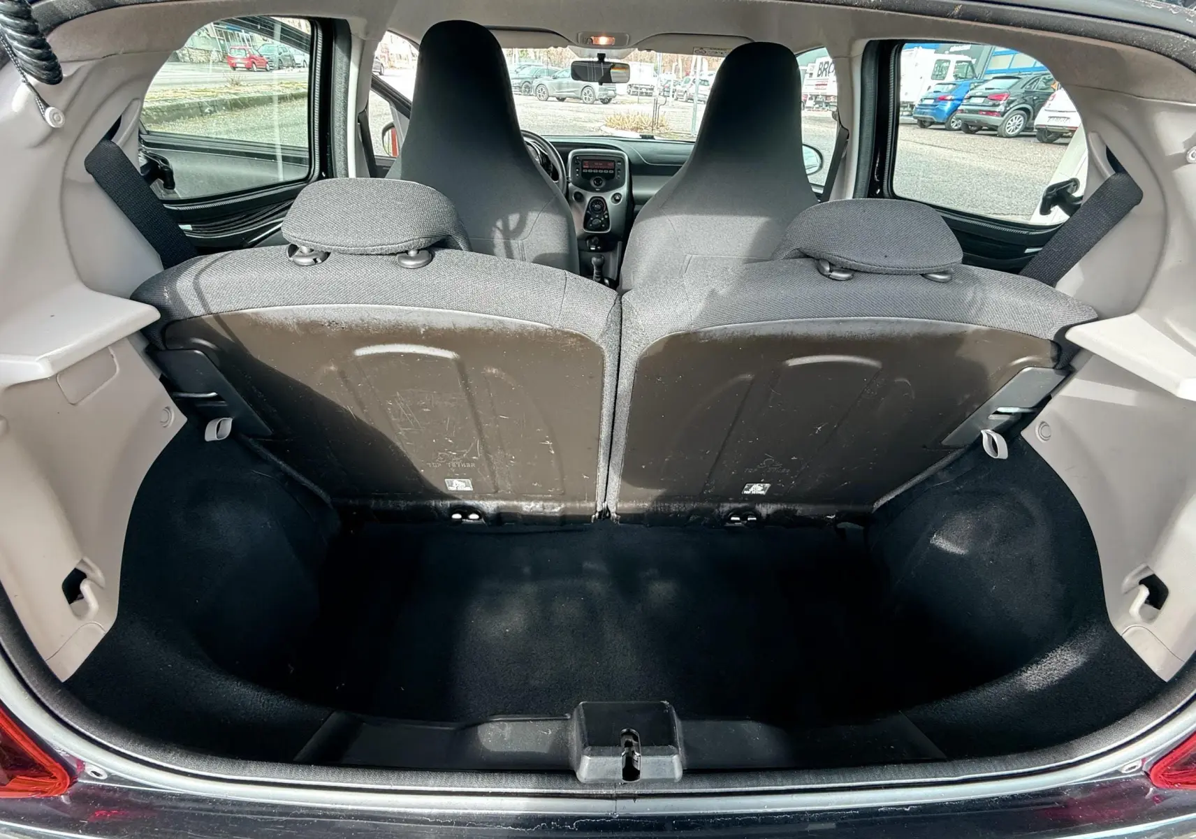 Vue depuis le coffre ouvert d'une Peugeot 108 noire, montrant l'espace de chargement et les dossiers arrière en tissu gris-noir.