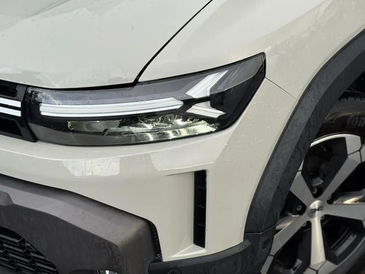 Gros plan sur l'avant droit du Dacia Duster 2024 beige Sandstone, mettant en valeur le phare LED et la jante alliage.