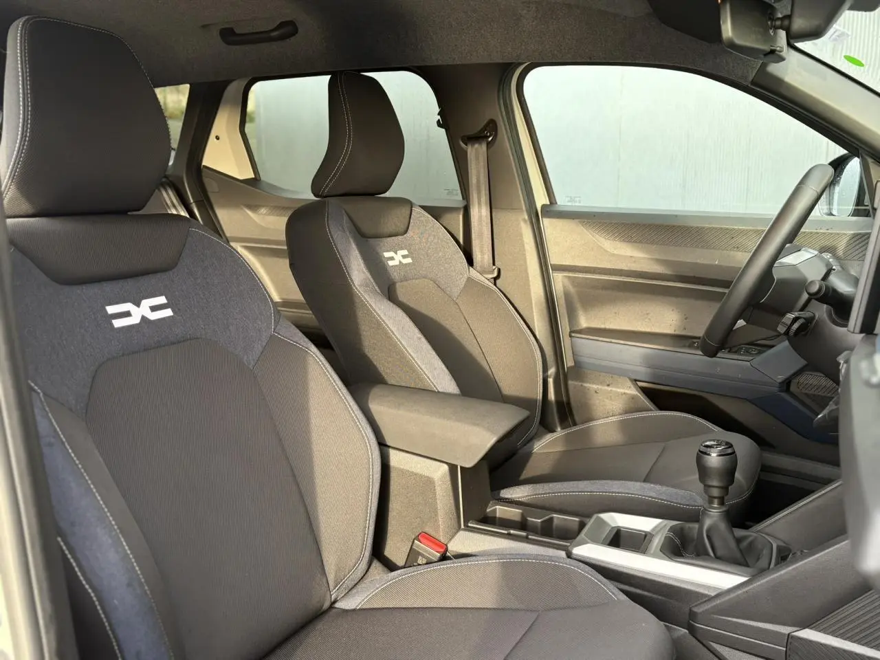 Vue intérieure côté droit du Dacia Duster 2024, sièges Denim avec logo Dacia, volant soft feel et levier de vitesses manuel.