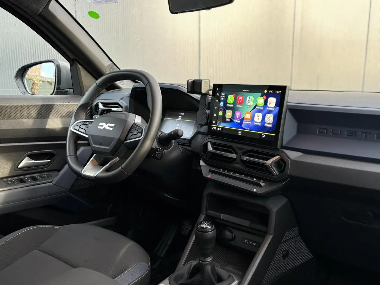 Vue intérieure côté conducteur du Dacia Duster 2024 beige Sandstone, avec volant multifonction et écran tactile central.