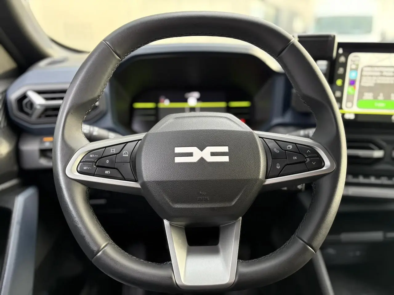 Gros plan sur le volant noir soft feel du Dacia Duster 2024 avec commandes intégrées et tableau de bord digital.