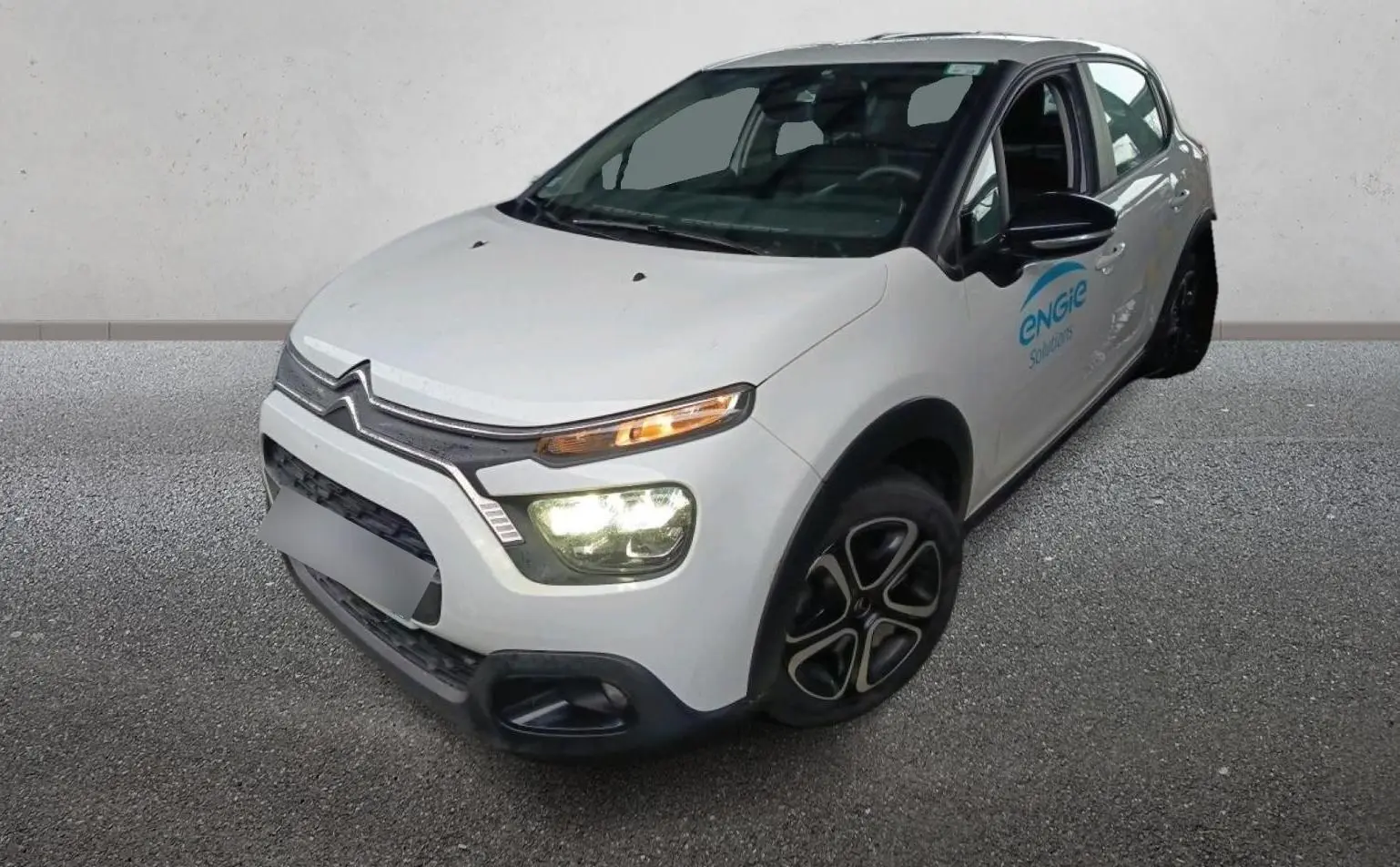 Vue 3/4 avant droit d'une Citroën C3 Société blanche avec phares allumés et logo Engie sur la porte avant.