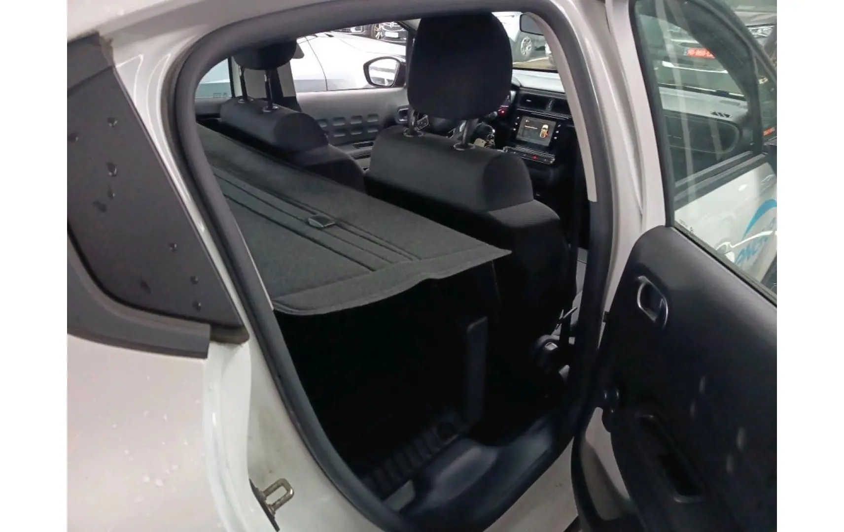 Vue intérieure côté droit de la Citroën C3 Société blanche 2021, montrant l’arrière avec tablette de coffre et sièges noirs.