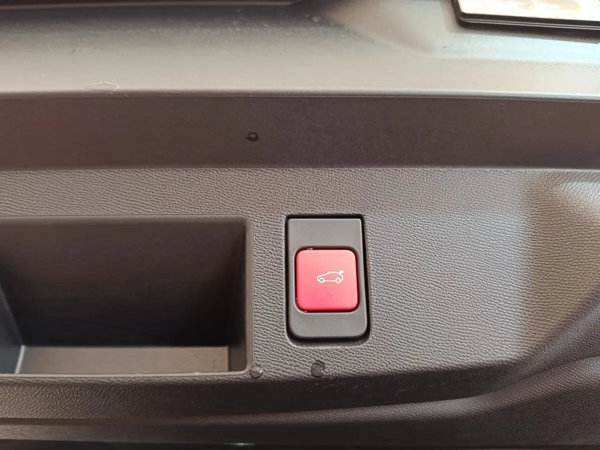 Bouton rouge d'ouverture électrique du coffre sur panneau intérieur noir, vue rapprochée sans indication extérieure visible.