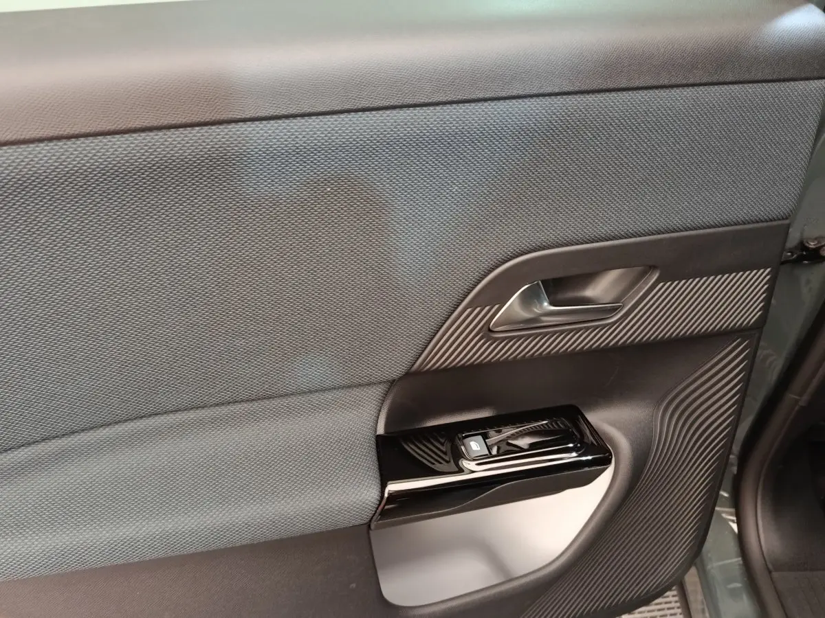 Gros plan sur la porte intérieure côté gauche de la Citroën C5 hybride verte, avec commande de vitre et insert texturé.