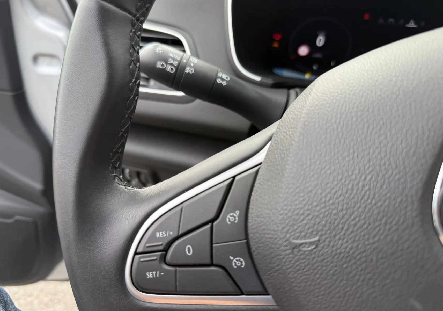 Gros plan sur le volant noir de la Renault Mégane Break 2024, montrant les commandes de régulateur de vitesse côté gauche.