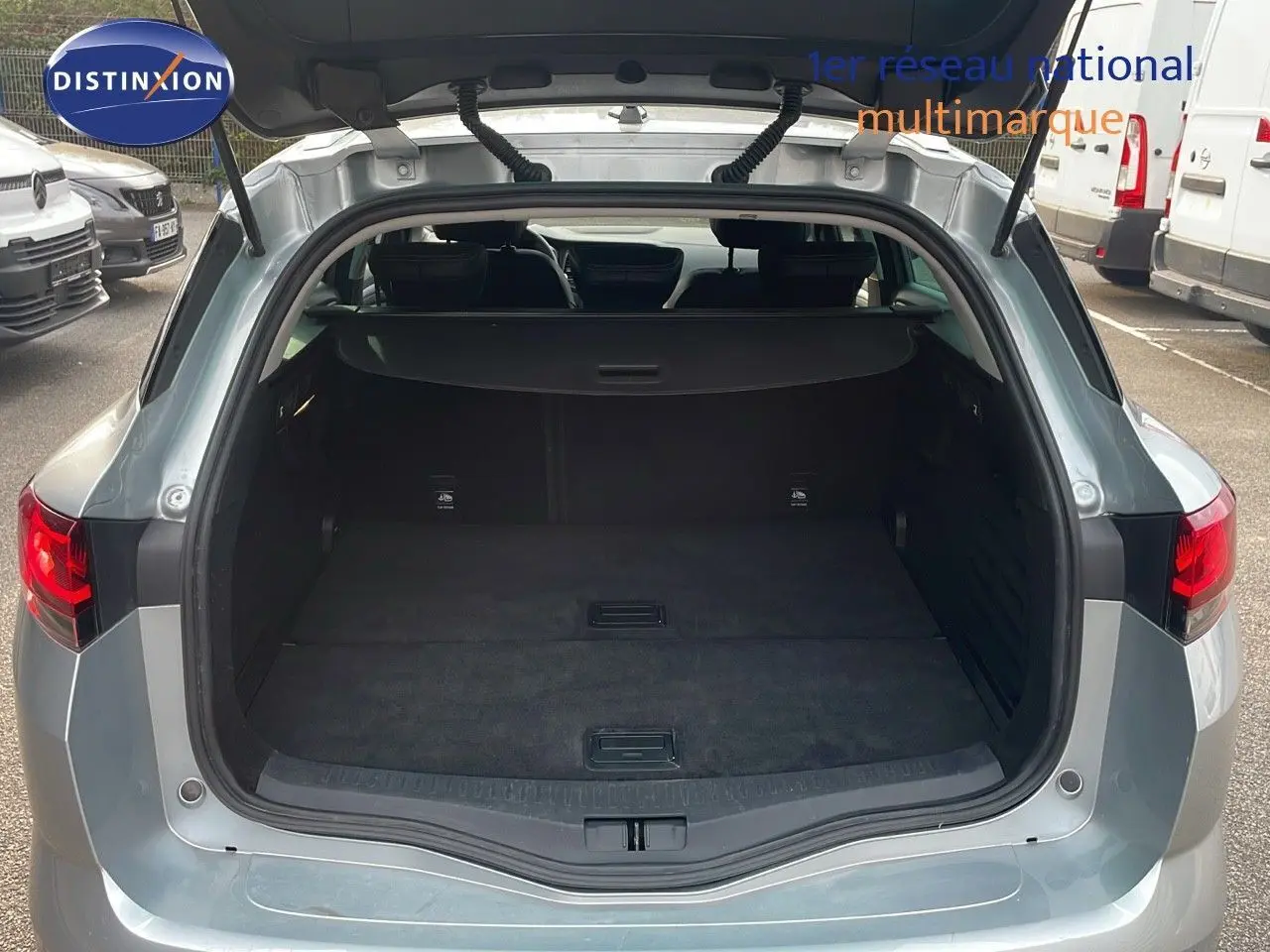 Coffre ouvert d'une Renault Mégane Break gris Highland Metal vue arrière en extérieur sur parking.