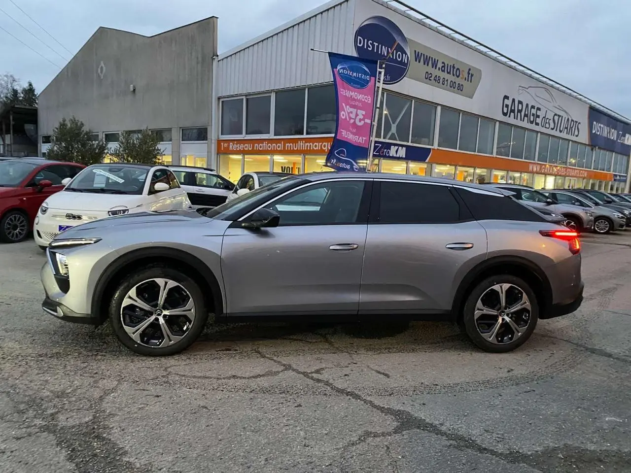 Profil côté gauche d'une Citroën C5 X gris Artense métal 2023 avec jantes alliage 19'' AeroX, feux arrière allumés.