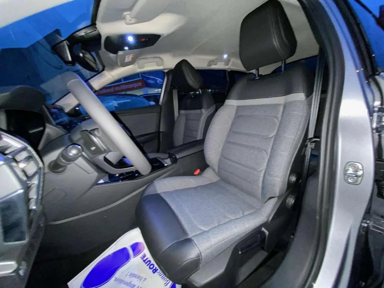 Vue intérieure côté conducteur de la Citroën C5 X 2023 gris Artense, sièges tissu gris avec appuie-tête noir.