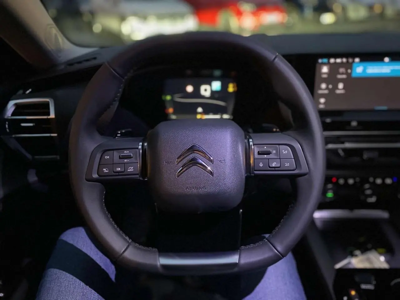 Volant en cuir noir avec commandes intégrées dans l'habitacle sombre d'une Citroën C5 X 2023, vue conducteur.