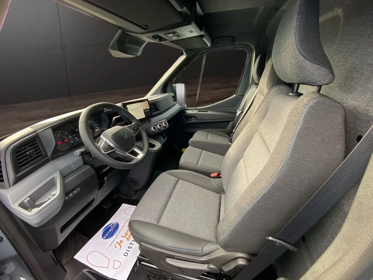 Vue intérieure côté conducteur du Renault Master 2025, montrant les sièges gris et le tableau de bord moderne avec écran tactile.