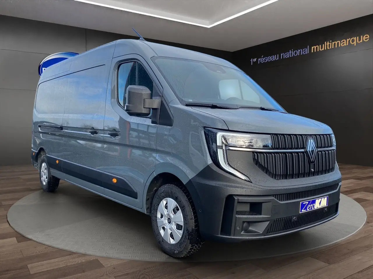 Vue 3/4 avant du Renault Master gris urbain 2025 avec calandre noire distinctive et jantes argentées, en showroom.