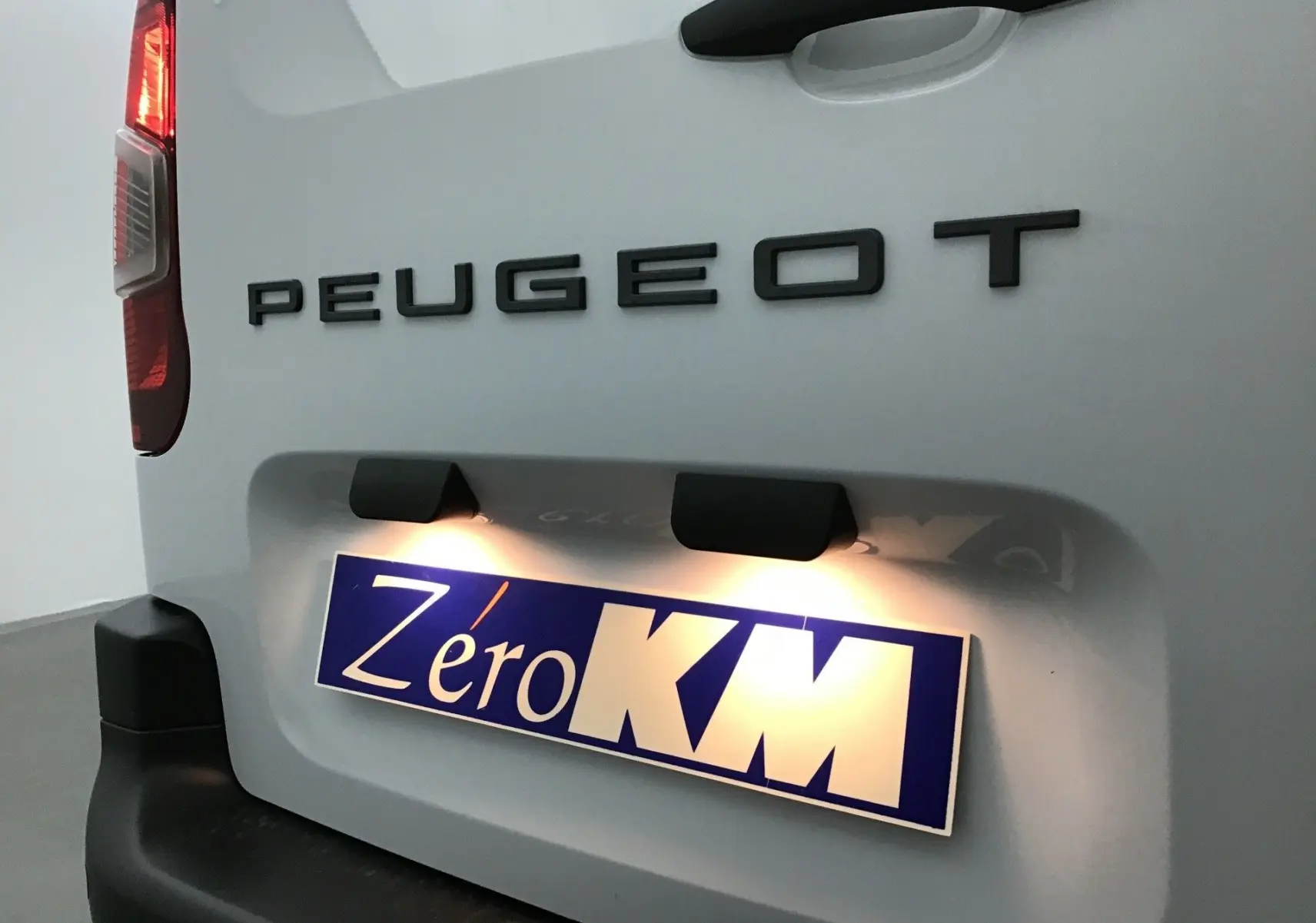 Gros plan sur l'arrière blanc du Peugeot Partner 2025 avec éclairage plaque et logo PEUGEOT en relief noir.