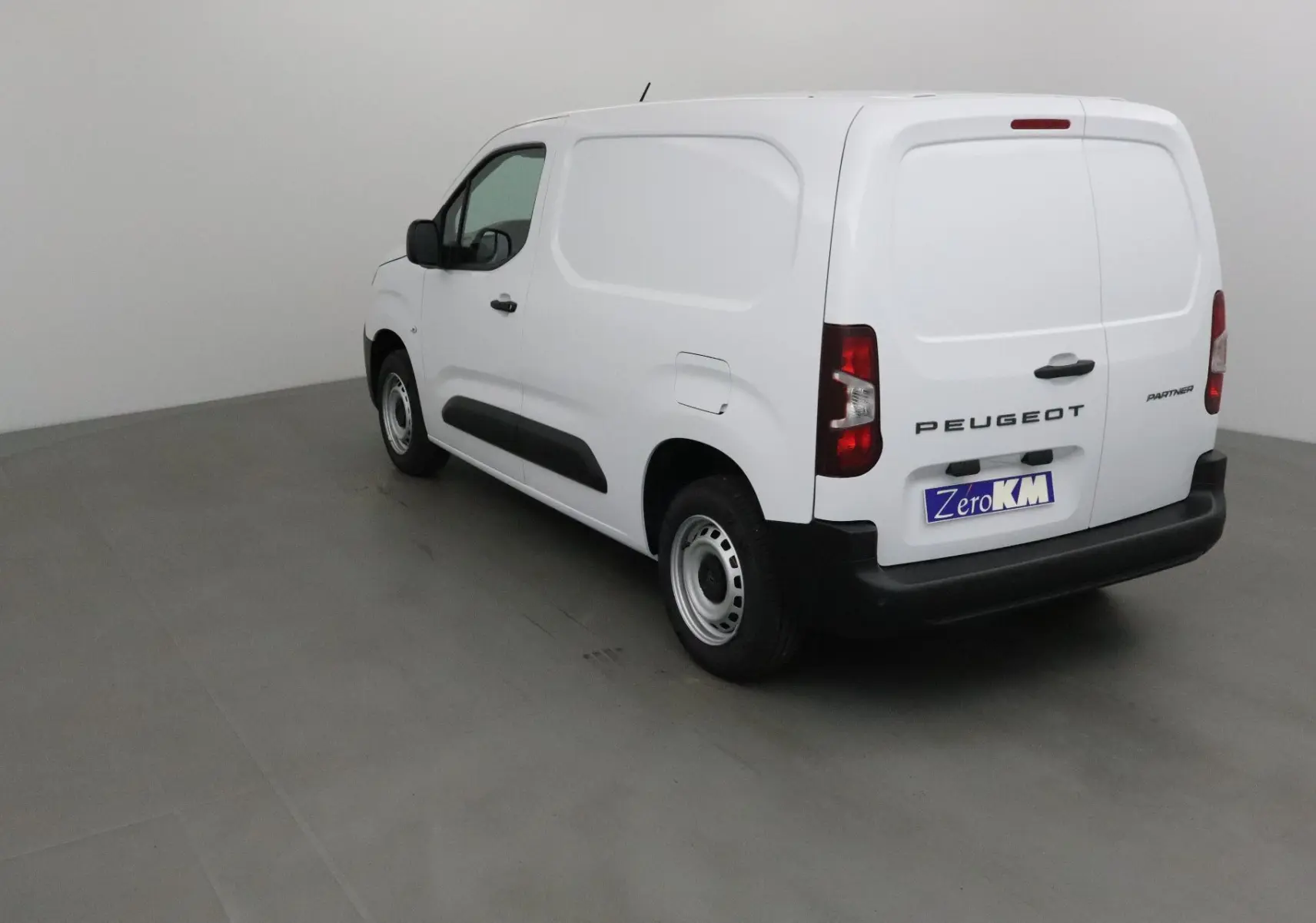Vue 3/4 arrière droite d’un utilitaire Peugeot Partner blanc avec porte latérale et hayon fermé dans un studio.