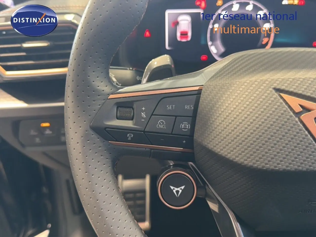 Gros plan sur le volant perforé gris avec logo CUPRA, boutons de commande et tableau de bord numérique en arrière-plan.