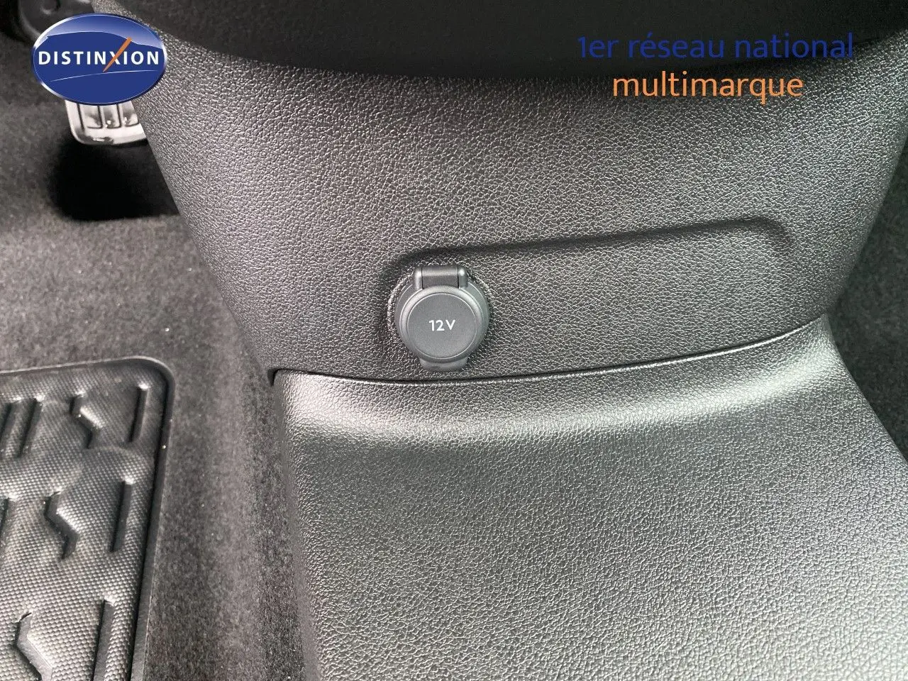 Prise 12V en gros plan sur la console centrale noire du Citroën Berlingo Fourgon blanc, vue intérieure rapprochée.
