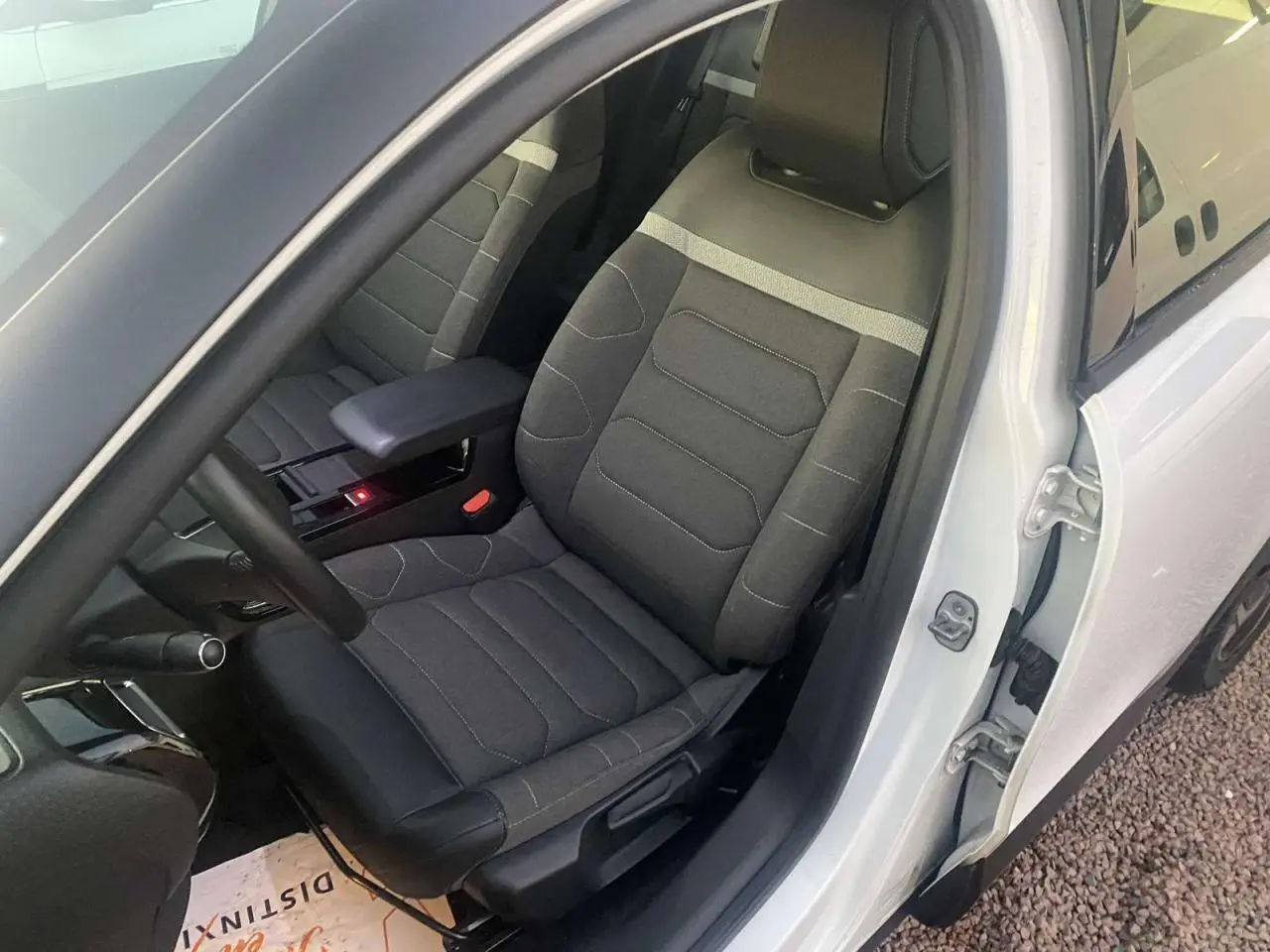 Vue intérieure côté conducteur d'une Citroën C4 blanche 2021, siège tissu gris avec accoudoir central ouvert.