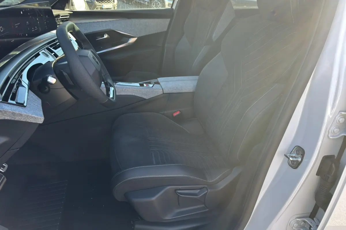 Vue intérieure côté conducteur du Peugeot 3008 Hybrid 136 GT Plus 2024 blanc okénite, sièges noirs avec surpiqûres et tableau de bord moderne.