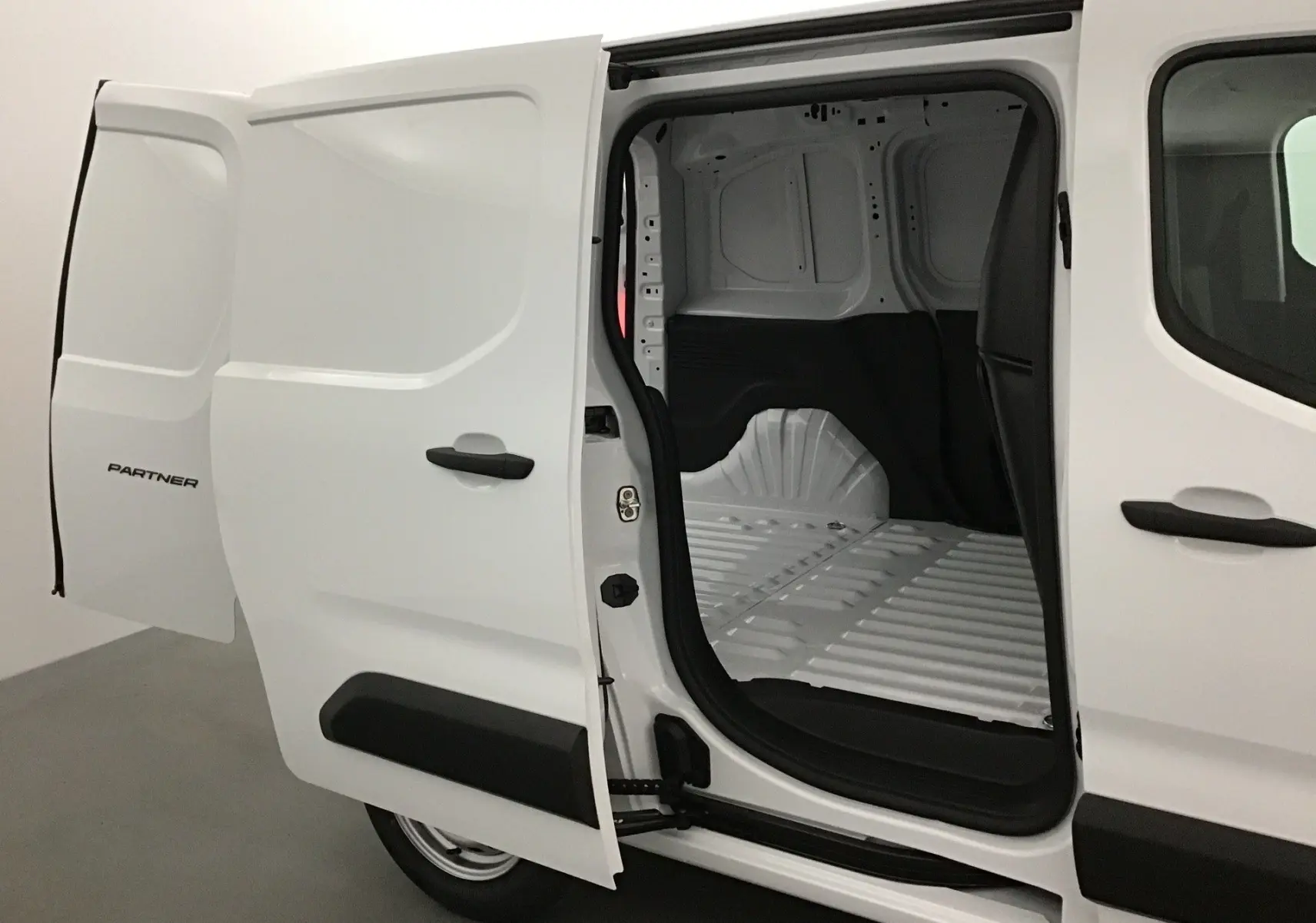 Vue latérale droite d’un Peugeot Partner blanc 2025 avec porte coulissante ouverte montrant l’espace de chargement vide.