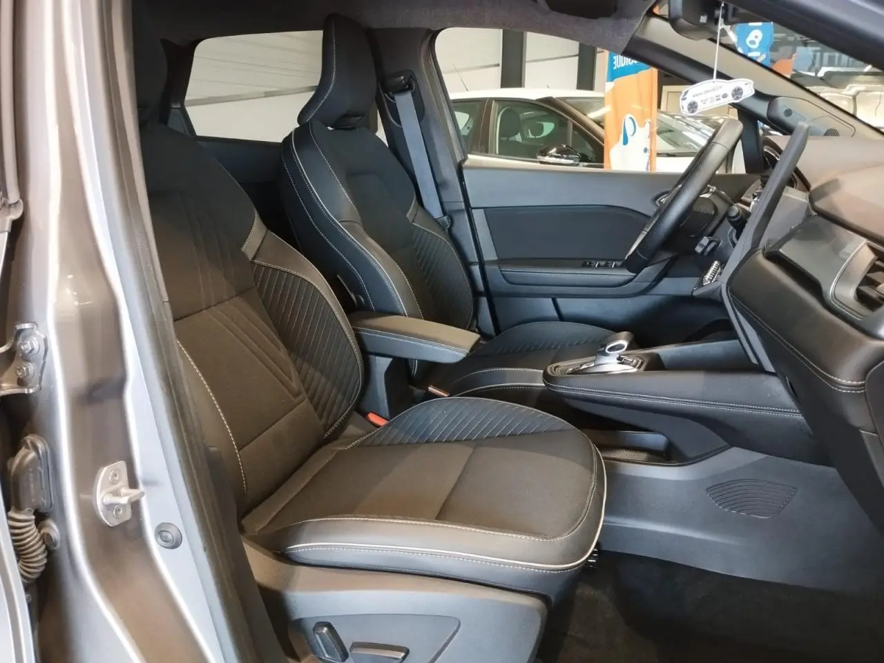 Vue intérieure côté gauche des sièges avant noirs avec surpiqûres blanches du Renault Symbioz 2025 Gris Cassiopée.