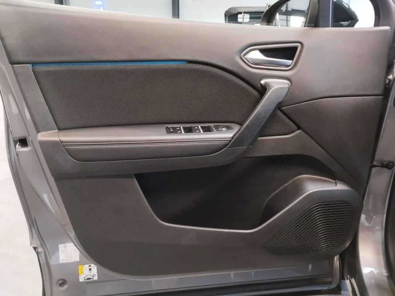 Porte avant gauche ouverte du Renault Symbioz 2025 gris Cassiopée, avec panneau noir et commandes de vitres intégrées.