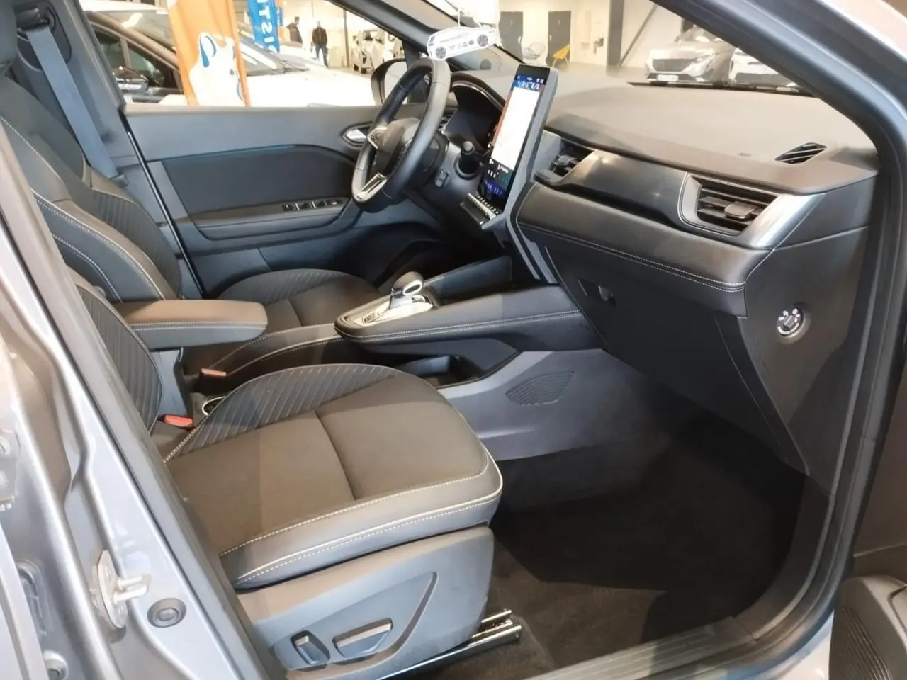 Vue intérieure côté conducteur de la Renault SYMBIOZ 2025 gris Cassiopée avec tableau de bord moderne et écran vertical.