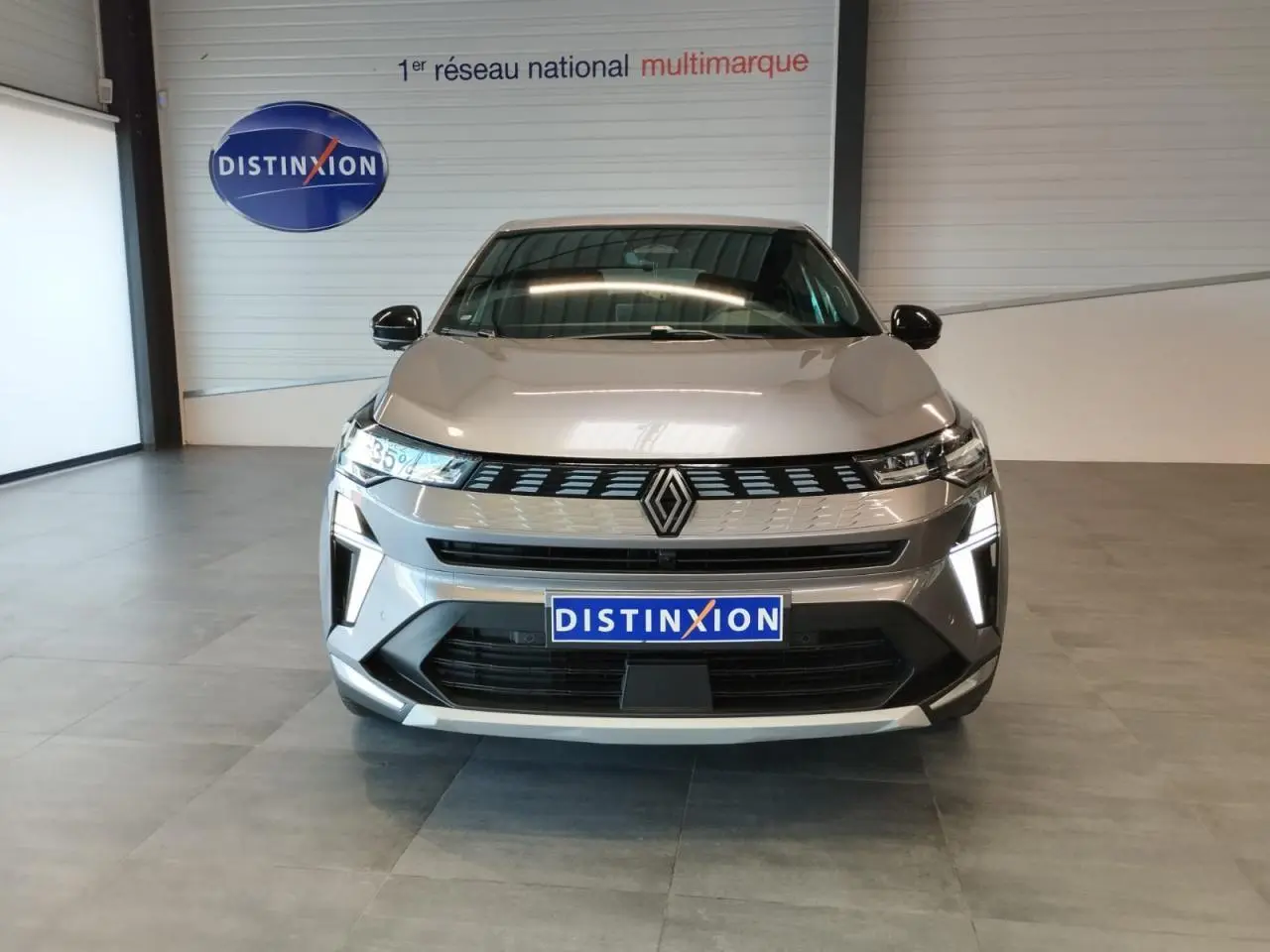 Vue frontale du Renault SYMBIOZ gris Cassiopée avec calandre noire et éclairage LED distinctif en intérieur showroom.
