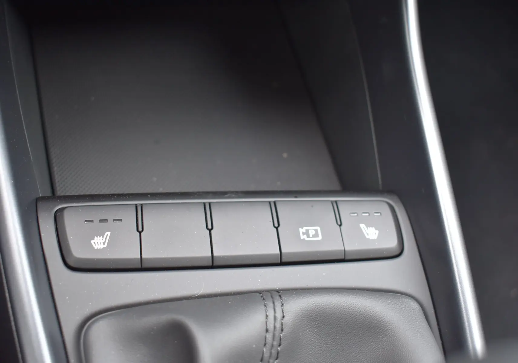Gros plan sur la console centrale de la Hyundai i20 2025, boutons de sièges chauffants et aide au stationnement visibles.